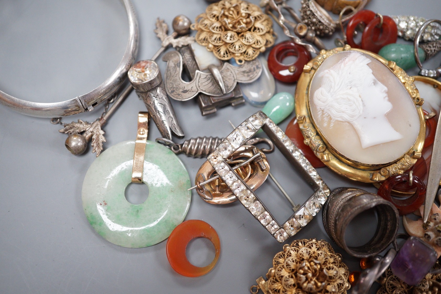 Assorted jewellery including jade pendant, yellow metal buckle brooch, modern silver hinged bangle, cameos, unmounted oval moonstone, agate set white metal buckle brooch, 800 standard paper knife etc.